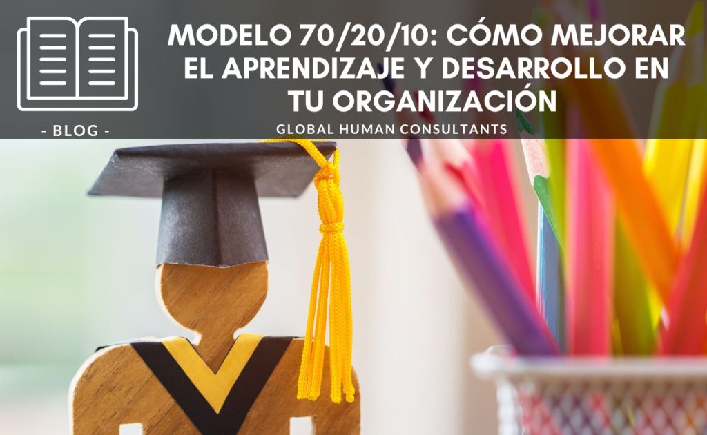 Banner de blog titulado 'Modelo 70/20/10: Cómo mejorar el aprendizaje y desarrollo en tu organización', de Global Human Consultants. La imagen muestra una figura de madera con birrete y cordón amarillo, simbolizando educación y aprendizaje, junto a un fondo desenfocado de lápices de colores en un recipiente, representando creatividad y desarrollo.